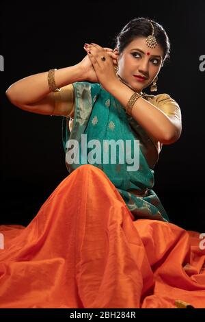 Danseuse Kathak assise avec élégance devant un fond sombre. Banque D'Images