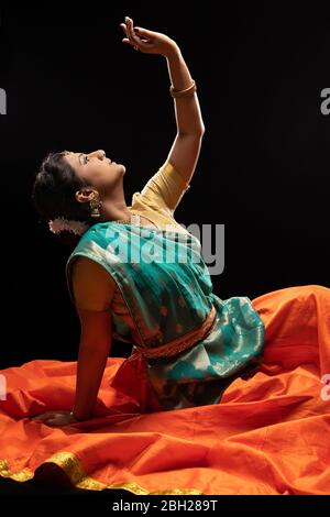 Danseuse Kathak assise avec élégance devant un fond sombre. Banque D'Images