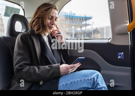 Femme d'affaires à l'arrière d'un taxi regardant le téléphone Banque D'Images