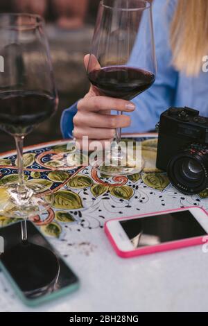 Gros plan de la femme à la table avec un verre de vin rouge, un appareil photo et des téléphones cellulaires Banque D'Images