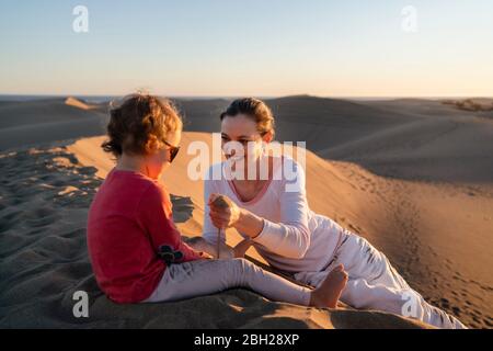 Mère et fille jouant avec le sable dans les dunes au coucher du soleil, Gran Canaria, Espagne Banque D'Images