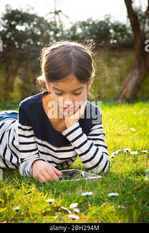 Portrait d'une petite fille couché sur un pré à l'aide d'une tablette numérique Banque D'Images