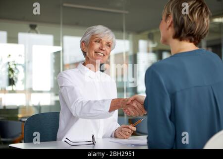 Two businesswomen shaking hands at desk in office Banque D'Images