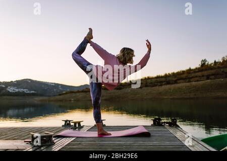 Jeune femme faisant du yoga sur une jetée, position de danseuse Banque D'Images