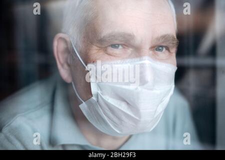 Portrait d'un homme âgé portant un masque à la maison, regardant par la fenêtre Banque D'Images