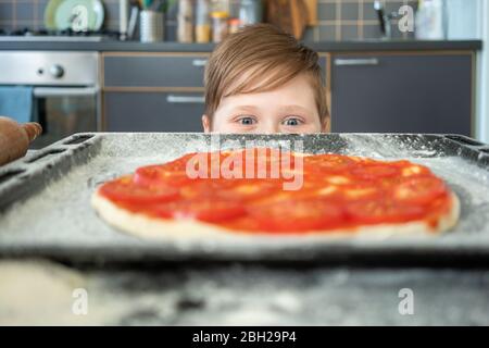 Garçon portant une pizza crue sur une plaque de cuisson Banque D'Images