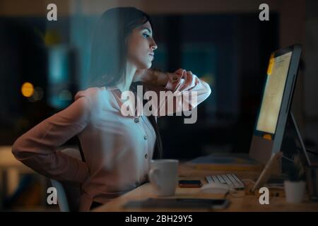 Jeune femme assise à un bureau au bureau ayant des douleurs au dos et au cou Banque D'Images