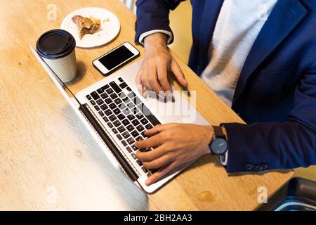 Vue rognée d'un homme d'affaires travaillant sur un ordinateur portable dans un café Banque D'Images