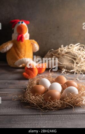 Les œufs de poulet brun et blanc nichent dans un nid de paille sur fond de bois. À côté d'un jouet de poulet. Orientation verticale Banque D'Images