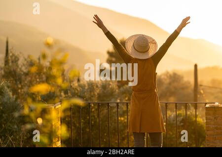 Femme profitant de la vue du coucher de soleil dans la campagne levant les armes, Orgiva, Andalousie, Espagne Banque D'Images