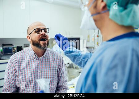 Médecin à l'hôpital prenant un écouvillon de la bouche du patient Banque D'Images