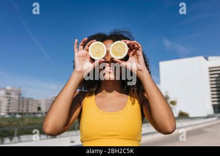 Portrait de la jeune femme en train de rire couvrant les yeux avec des moitiés de citron Banque D'Images