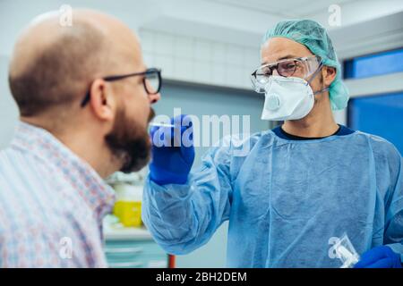 Médecin à l'hôpital prenant un écouvillon de la bouche du patient Banque D'Images