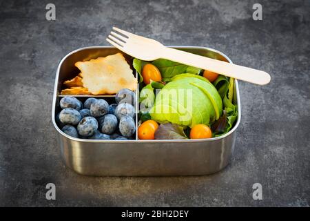 Boîte à lunch avec tranches d'avocat, tomates jaunes, craquelins, bleuets et salade verte Banque D'Images