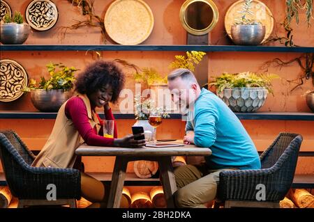 Homme et femme prenant un verre dans un restaurant, en utilisant un smartphone