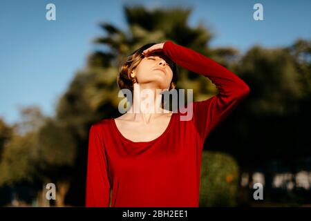 Portrait d'une jeune femme aux yeux fermés portant une robe rouge dans un parc Banque D'Images