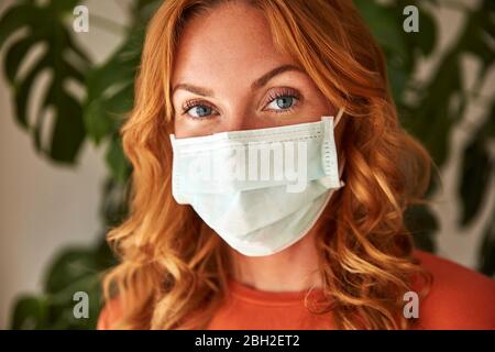 Portrait d'une femme aux cheveux rouges portant un masque de protection à la maison Banque D'Images