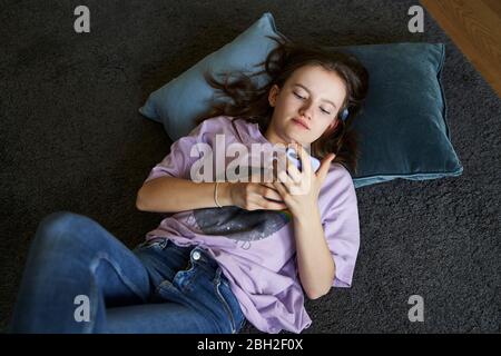 Portrait d'une fille qui se trouve sur le sol à la maison et qui regarde un smartphone Banque D'Images