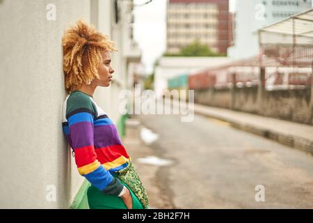 Portrait d'une jeune femme dans une coiffure afro penchée sur un mur dans la ville