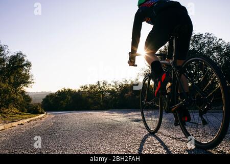 Gros plan d'un athlète qui fait du vélo sur la route de campagne au coucher du soleil Banque D'Images