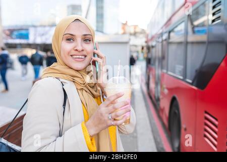 Portrait d'une jeune femme souriante au téléphone attendant à l'arrêt de bus Banque D'Images