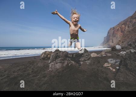 Un petit garçon sautant pour la joie sur une plage rocheuse
