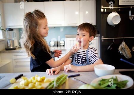Fille nourrissant son petit frère avec des pommes de terre dans la cuisine Banque D'Images