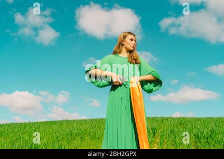 Jeune femme portant une robe verte debout dans un champ avec des ciseaux et un ruban Banque D'Images