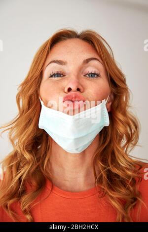 Portrait d'une femme aux cheveux rouges avec des lèvres baiseuses sur un masque protecteur Banque D'Images