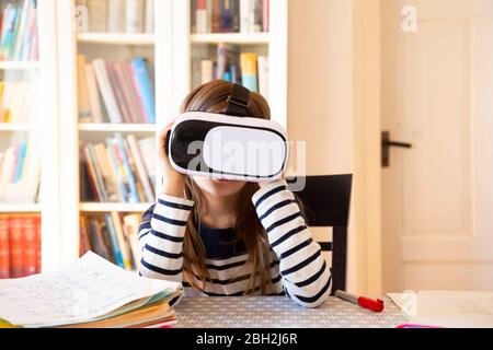 Fille assise à la table à la maison à l'aide de lunettes de réalité virtuelle Banque D'Images