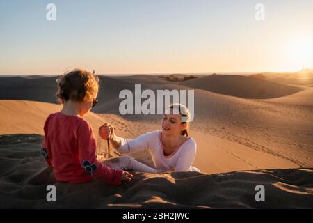 Mère et fille jouant avec le sable dans les dunes au coucher du soleil, Gran Canaria, Espagne Banque D'Images