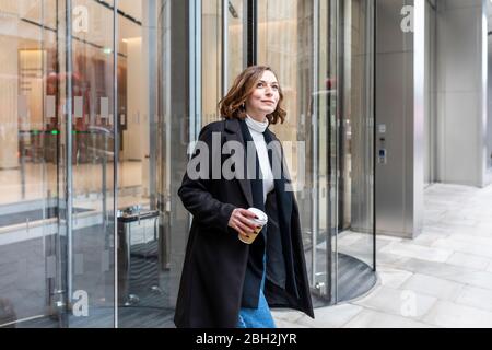 Femme dans la ville en sortant de la porte tournante, Londres, Royaume-Uni Banque D'Images