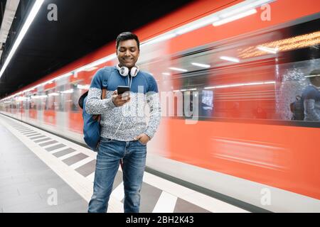 Homme souriant utilisant un smartphone dans la station de métro Banque D'Images