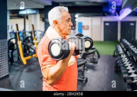 Homme senior levant des haltères dans la salle de gym Banque D'Images