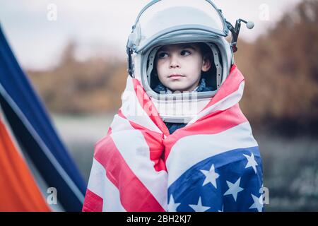 Portrait d'un petit garçon enveloppé dans un drapeau américain portant un casque d'espacement Banque D'Images