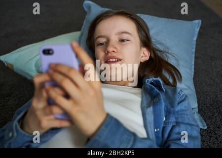 Portrait d'une fille qui se trouve sur le sol à la maison et qui regarde un smartphone Banque D'Images