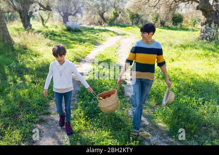 Mère et fille marchant sur un chemin rural portant un panier avec des oranges Banque D'Images