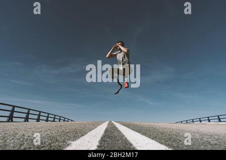 Athlète handicapé avec prothèse de jambe sautant sur une route Banque D'Images