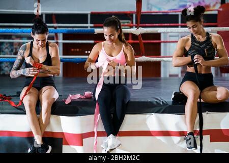 Trois jeunes femmes nouant le bandage autour de ses mains dans le club de boxe Banque D'Images