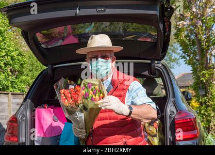 Angleterre Royaume-Uni. 2020. Homme âgé portant un masque et des gants déchargeant la boutique hebdomadaire et quelques fleurs colorées d'une voiture. Pendant Covid-19. Banque D'Images