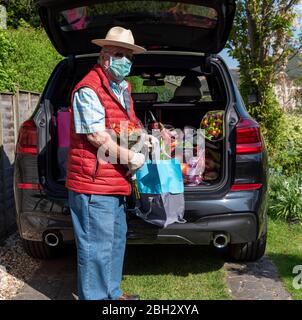 Angleterre Royaume-Uni. 2020. Homme âgé portant un masque et des gants déchargeant la boutique hebdomadaire et quelques fleurs colorées d'une voiture. Pendant Covid-19. Banque D'Images