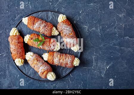Des gâteaux de cheminée hongrois remplis de crème au beurre, décorés de menthe fraîche sur le dessus, servis sur un plateau de service noir, vue de dessus, espace libre pour le t Banque D'Images
