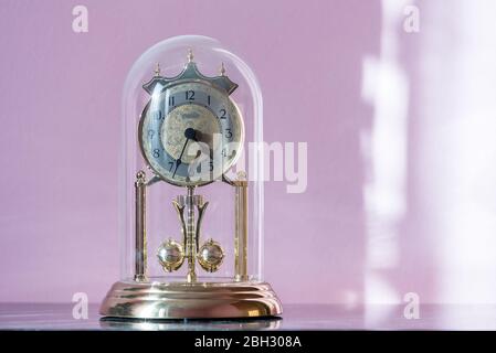 Horloge Mantel avec dôme en verre et balancier rotatif. Horloge d'époque avec mécanisme oscillant sur un vieux Cupboard poussiéreux éclairé par le soleil du matin Banque D'Images