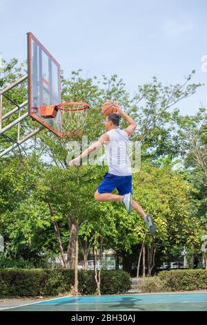 Le basket-ball dans la main man jumping jeter un arbre dans l'arrière-plan de basket-ball park. Banque D'Images