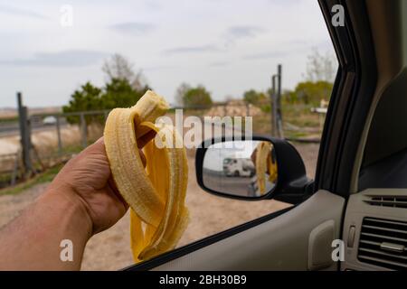 Conducteur de voiture mangeant la banane par l'autoroute et reflet de la banane dans le miroir Banque D'Images