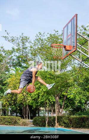 Le basket-ball dans la main man jumping jeter un arbre dans l'arrière-plan de basket-ball park. Banque D'Images