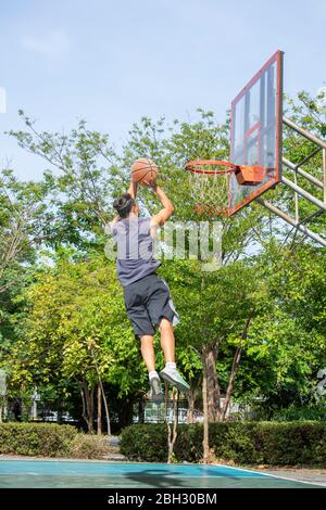 Le basket-ball dans la main man jumping jeter un arbre dans l'arrière-plan de basket-ball park. Banque D'Images