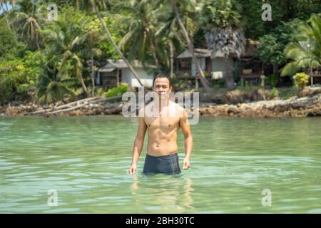 Les hommes asiatiques nager dans la mer des rochers et des arbres en arrière-plan. Banque D'Images