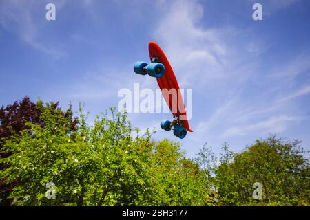 Un skateboard rouge qui se fait voler, gainst un ciel bleu parfait et des arbres verts Banque D'Images