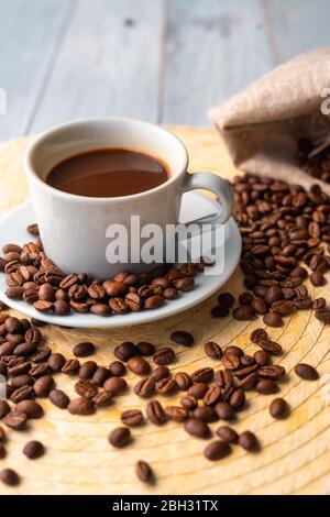 Tasse blanche et soucoupe avec café et entourée de grains de café rôtis sur une table en bois et un sac Banque D'Images